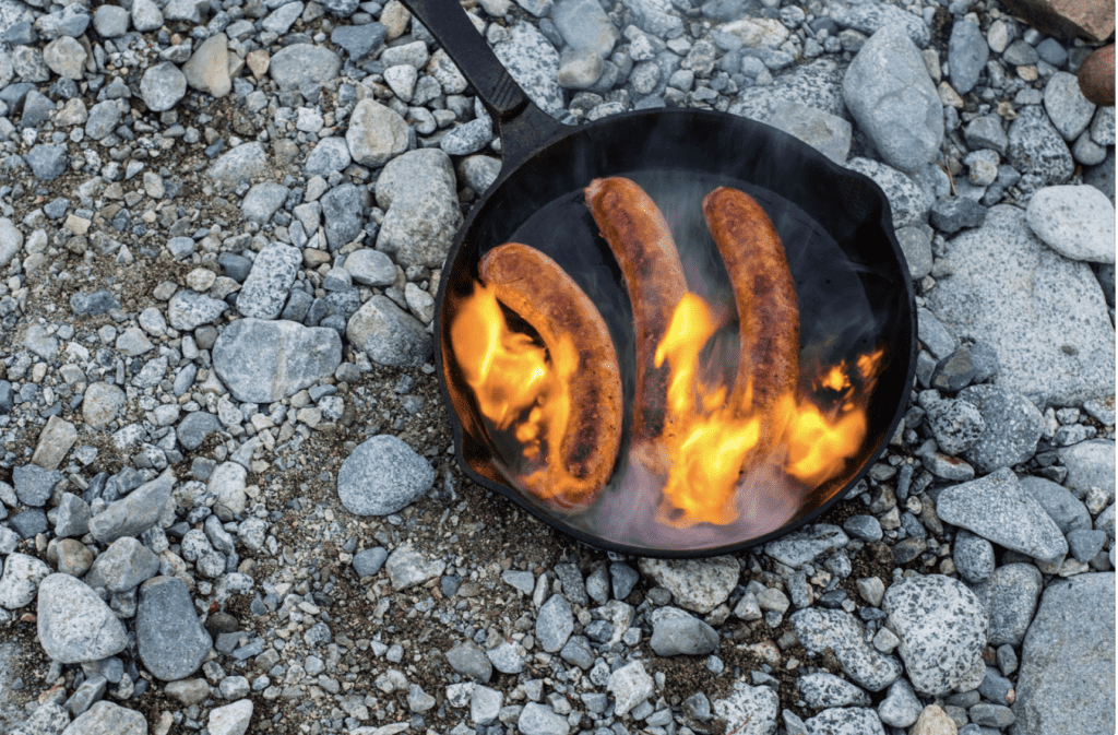 Cooking sausages in cast iron skillet on campfire