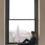 a woman sitting on window sill at the top of the rock in new york city