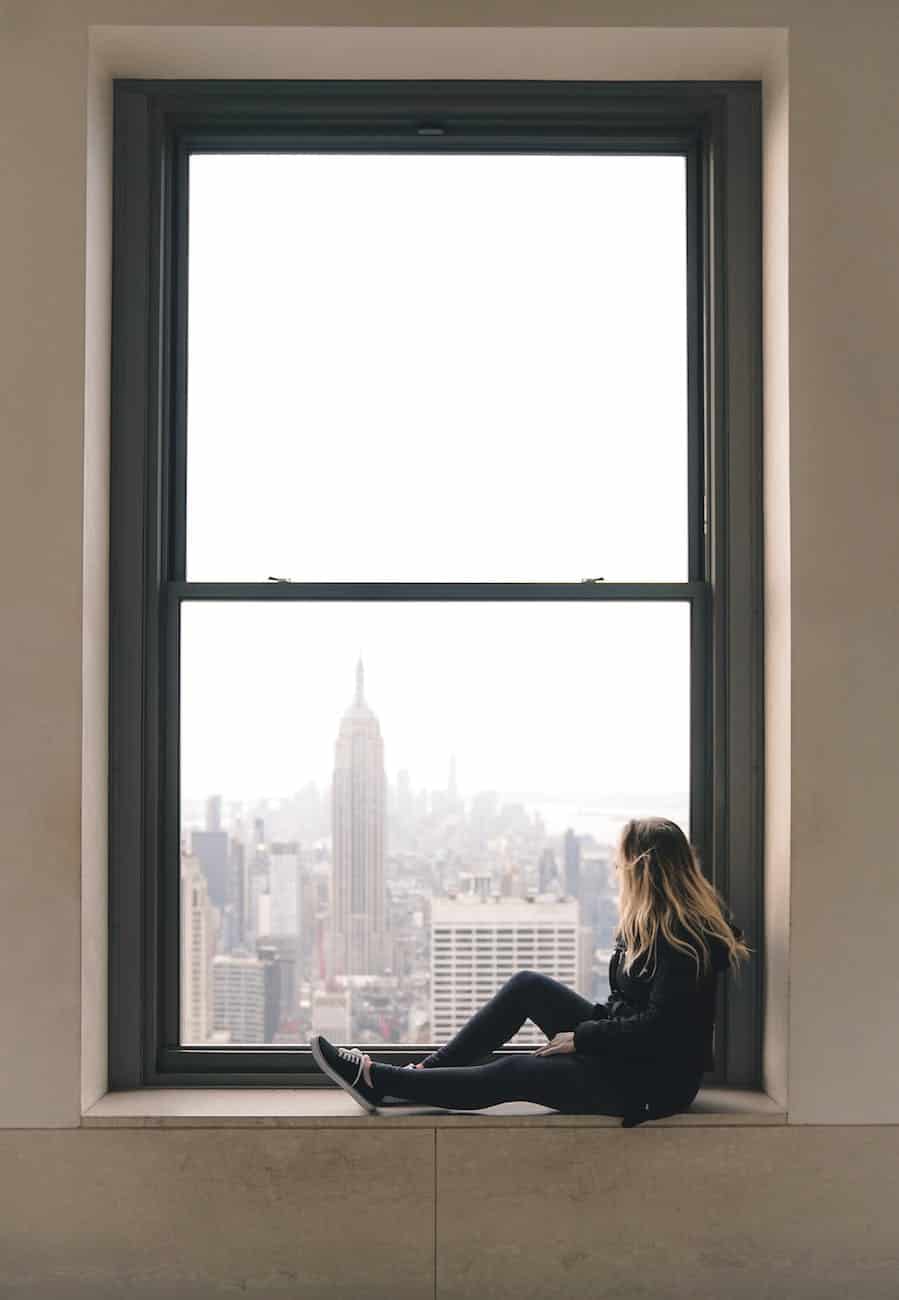 a woman sitting on window sill at the top of the rock in new york city