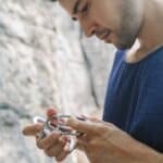 man in blue tank top looking at carabine hooks by a rock